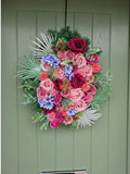 Blooming Proper Miss Rosalina Christmas wreath featuring vibrant pink, red, and purple flowers with silver foliage.