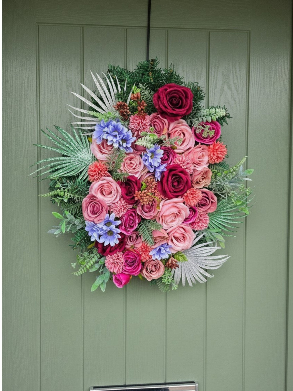 Blooming Proper Miss Rosalina Christmas wreath featuring vibrant pink, red, and purple flowers with silver foliage.